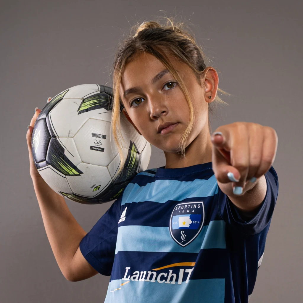 young girl holding soccer ball and pointing at the camera.
